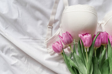 Gentle white lace bra on the bed with tulips. Women tender lingerie, underwear. Top view, close up. Flat lay, beauty blog or social media minimal concept. Present for Valentines, Women&rsquo;s day