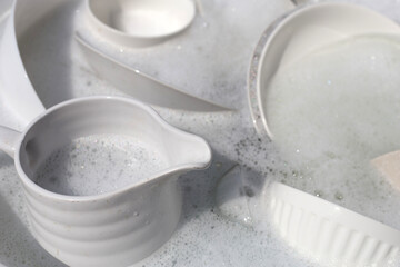 Dishes and bowls in water and bubbles of dishwashing liquid. Kitchen work