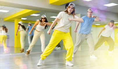 Energetic young girl wearing cap engaging in breakdance in dance studio. Teenagers training Toprock moves