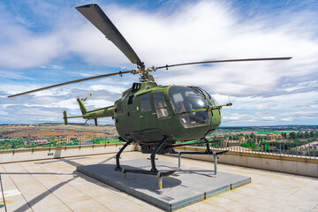 Helicóptero militar antiguo posado en la azotea de un edificio de la ciudad un día soleado con cielo azul y nubes.