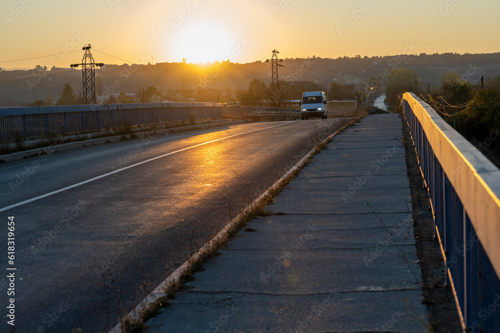 Wall mural a white minivan crosses the overpass over the highway. beautiful sunset in the background. white mod