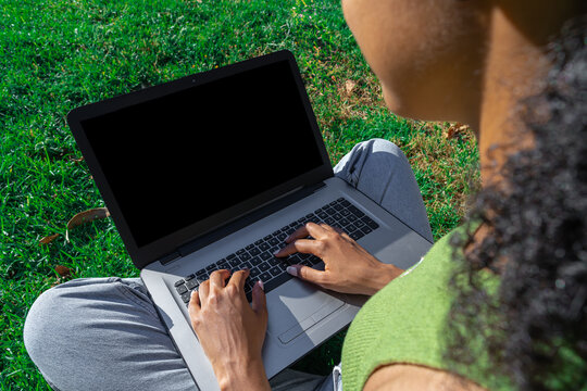 Manos de mujer sentada en el parque manejando una computadora port&aacute;til colocada sobre sus piernas cruzadas, La pantalla de la computadora esta en negro para espacio para testo.