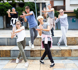 Group of modern teenagers performing street dance choreography outdoors in summer.