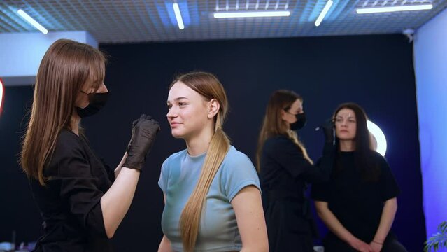 Beauticians in masks working with clients in salon. Women having cosmetology procedures on eyebrows. Permanent eyebrow make up.