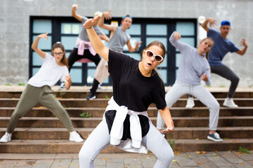 Modern teen girl krump dancer posing during performance with group on summer city street.