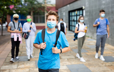 Young student in a protective mask going to college down the city street