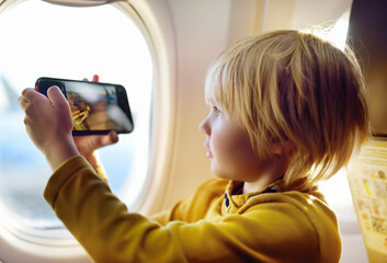 Little boy is taking a shot view of airfield from illuminator plane by smartphone.