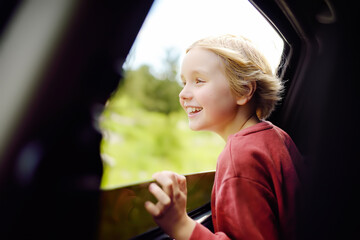 Cute preteen boy looking out through window of car during family road trip and enjoy of pleasant...