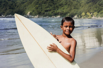 latin child boy with surfboard on the beach in Mexico Latin America, hispanic people surfing in...