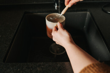 Fototapeta na wymiar Mugs cleaning with a brush.Eco housekeeping and dishwashing.Zero waste. hands wash a ceramic mug with a wooden brush with natural bristles over a black sink .