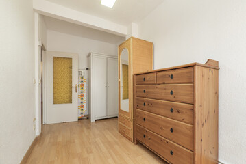 Room with a wooden sideboard of drawers, a narrow wicker cabinet with a mirror