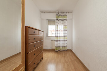 Room with a sideboard of wooden drawers, a narrow wicker wardrobe with a mirror