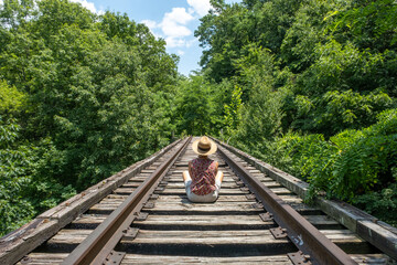 Fototapeta premium Rear view of a Caucasian woman on railroad tracks in the country woods on a sunny day.