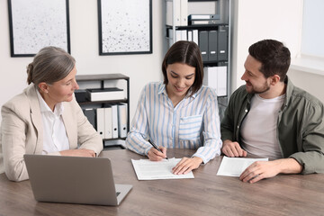 Young couple consulting insurance agent about pension plan at wooden table indoors