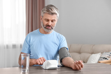 Man measuring blood pressure at table indoors