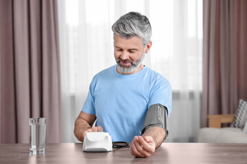 Man measuring blood pressure at table indoors