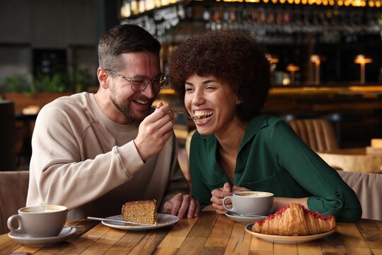 International dating. Handsome man feeding his girlfriend with cake in cafe