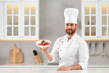 Happy chef presenting delicious dish at marble table in kitchen