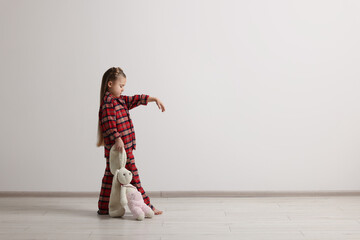 Girl in pajamas with toy bunny sleepwalking indoors, space for text