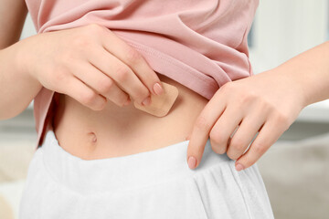 Fototapeta na wymiar Woman applying contraceptive patch onto her body indoors, closeup