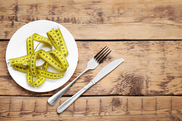 Plate with measuring tape on wooden table, flat lay and space for text. Weight loss concept