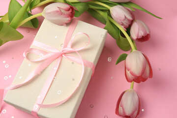 Beautiful gift box with bow, tulips and confetti on pink background