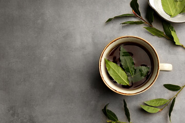 Cup of freshly brewed tea with bay leaves on grey table, flat lay. Space for text