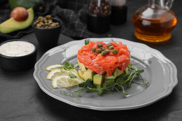 Delicious salmon tartare served with avocado and lemon on dark table
