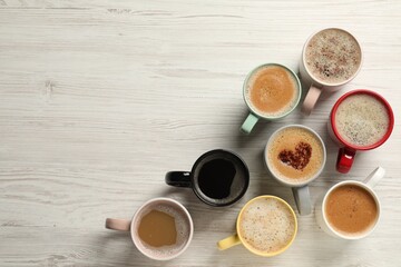 Many cups with different aromatic coffee on white wooden table, flat lay. Space for text