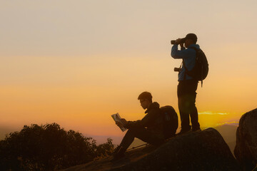 Two tourists with backpacks enjoying sunset on top of a mountain