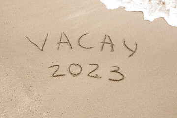 Word vacay 2023 written on the sand