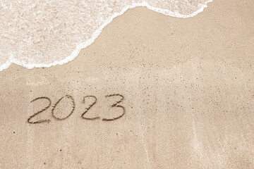 Inscription on the beach saying 2023 with a wave