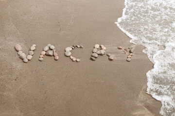 Word vacay written with pebble stones on the beach with a wave
