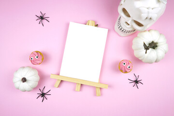 Pink Halloween table number easel with 5x7 card mockup. Trick or treat party supplies stationery styled with white skull, pumpkins, black spiders, and spooky cupcakes. Negative copy space.