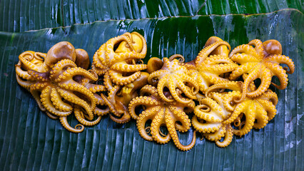 grilled baby octopus cooked yellow sauce on banana leaf in street food market