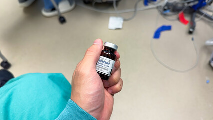 hand holds a syringe amidst IV drips and medications, symbolizing medical care, treatment, and the use of drugs in a hospital setting