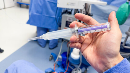 hand holds a syringe amidst IV drips and medications, symbolizing medical care, treatment, and the use of drugs in a hospital setting