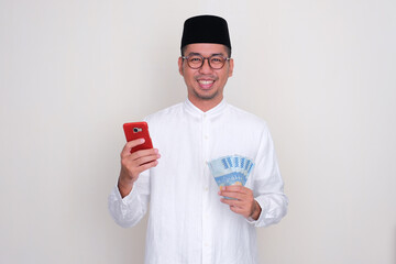 Moslem Asian man smiling happy while holding mobile phone and money