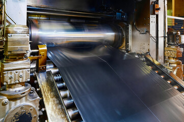 A wide belt of raw rubber compound moves along a roller conveyor. Plant for the production of car...