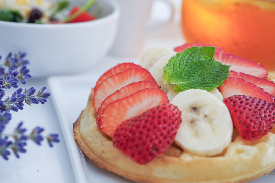 A Plate of Waffles toped with Strawberries and Bananas, small salad for Break