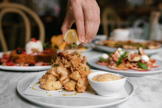 Squeezing lemon over deep fried calamari seafood on plate in restaurant.
