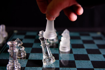 Checkmate - Chessboard with hand executing a checkmate move. Glass pieces. Selective focus.