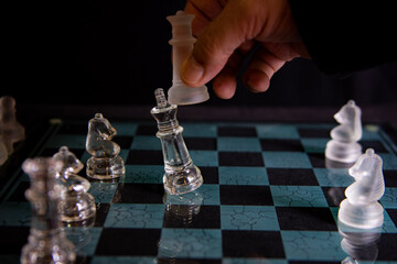 Checkmate - Chessboard with hand executing a checkmate move. Glass pieces. Selective focus.