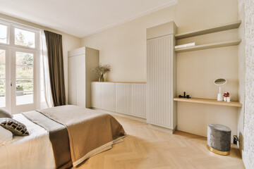 a bedroom with wood flooring and white wallpapers on the walls in front of the bed, there is a large window