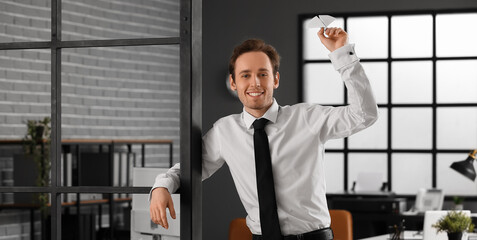 Happy young businessman throwing paper plane in office
