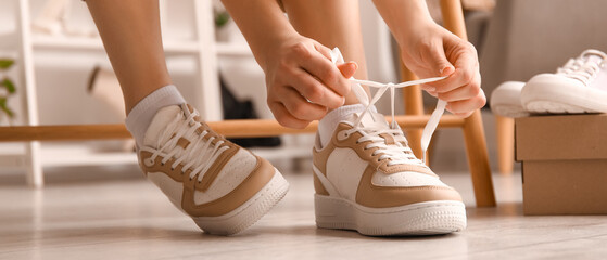 Woman in stylish sneakers tying shoe laces in shop - Powered by Adobe