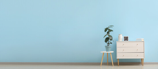 Stylish white chest of drawers with clock and houseplant on table near light blue wall. Banner for design