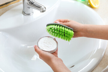 Woman cleaning white ceramic sink with brush and baking soda, closeup - obrazy, fototapety, plakaty