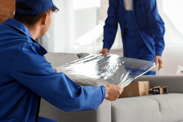 Male movers wrapping sofa with stretch film in room, closeup