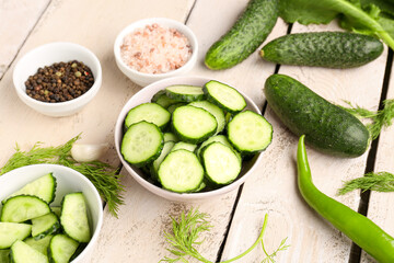 Bowls with pieces of fresh cucumber on light wooden background